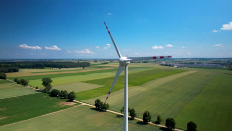 close-up of industrial wind turbine with rotating blades over green patchy grain agricultural fields - aerial parallax orbiting