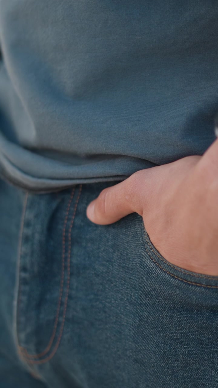 Close up of man wearing blue jeans with hands in pockets showing denim fabric texture and stitching details. subject remains stationary emphasizing casual attire and relaxed posture