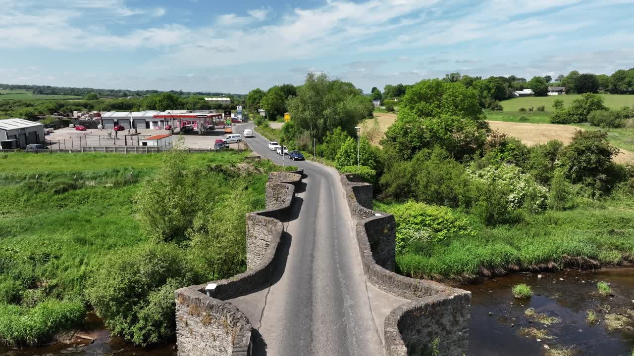 Clady Bridge, County Tyrone, Northern Ireland, June 2023. Drone approach tracking following car zooming away into distance as people wait on the other side to cross the River Finn.