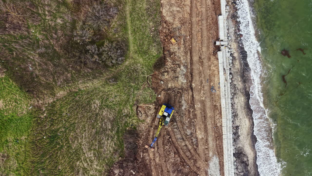Construction work is taking place near the shoreline on a cloudy day with heavy machinery operating along the water's edge