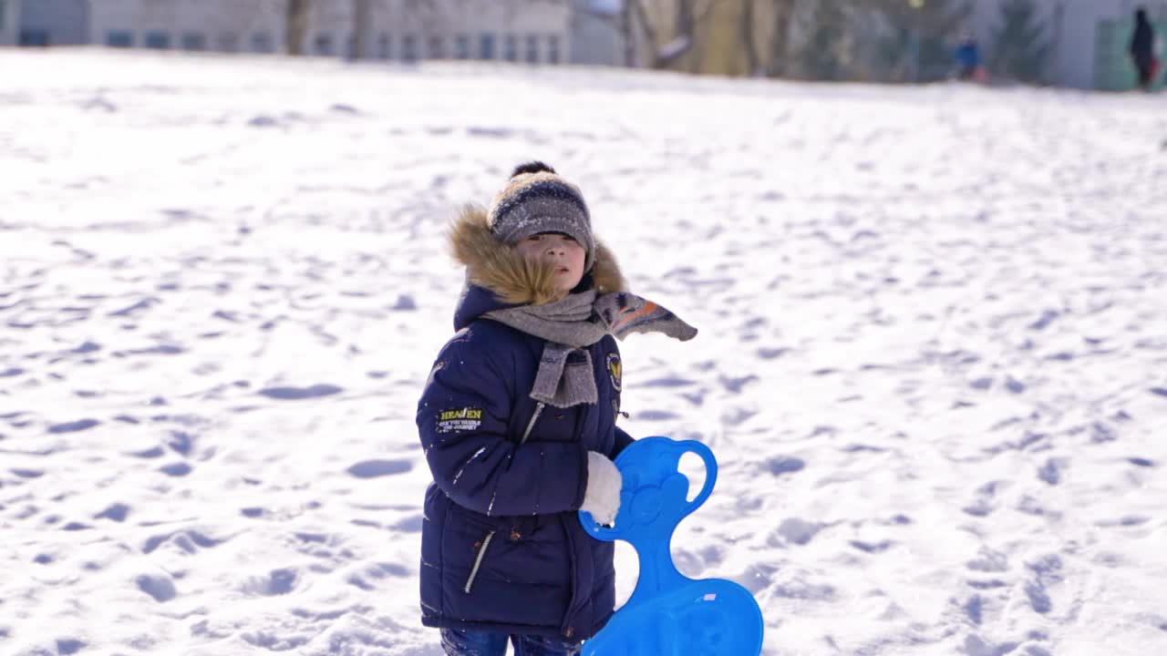 child boy having fun, playing and laughing on snowy winter walk in nature. Frost winter season.Cute little boy with saucer sleds outdoors on winter day, ride down the hills, winter games and fun