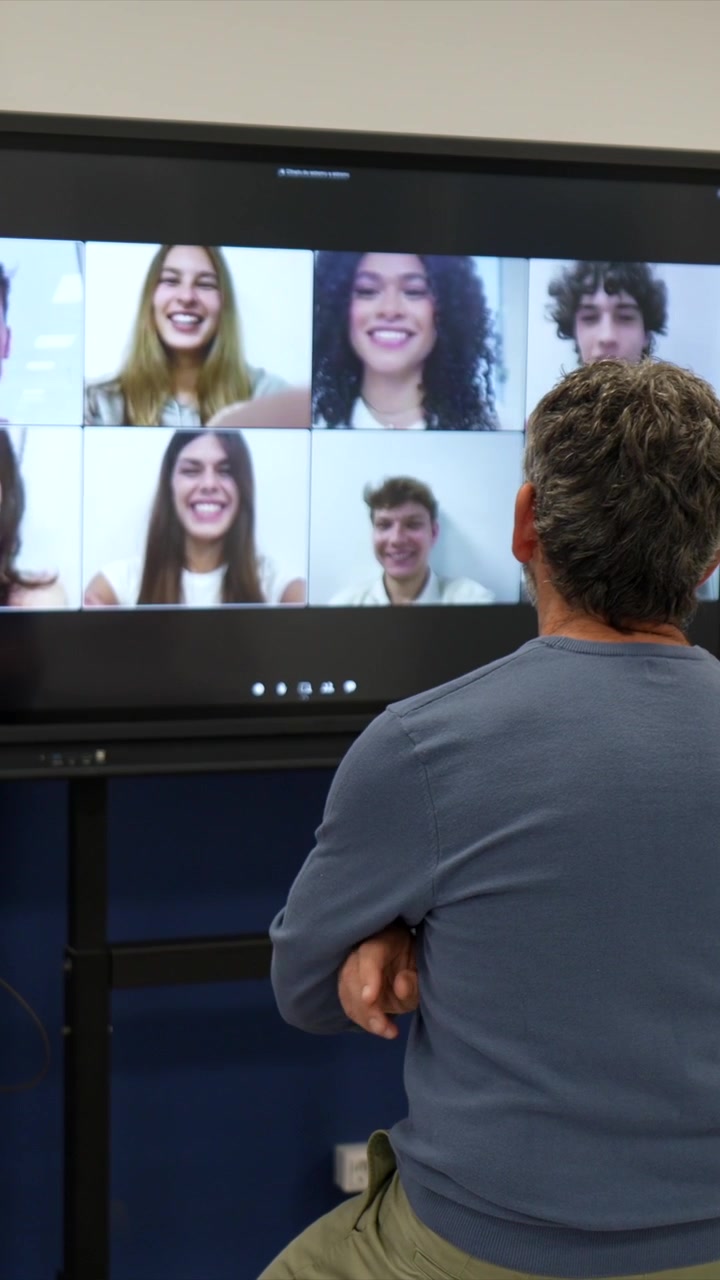 Uomo che guarda una videoconferenza con più giovani su un grande schermo.