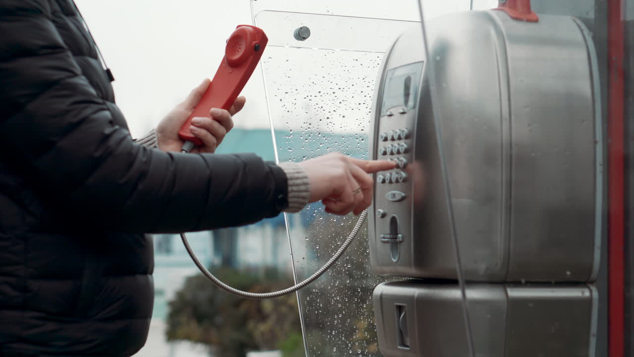 mujer haciendo una llamada desde un teléfono público en un día lluvioso