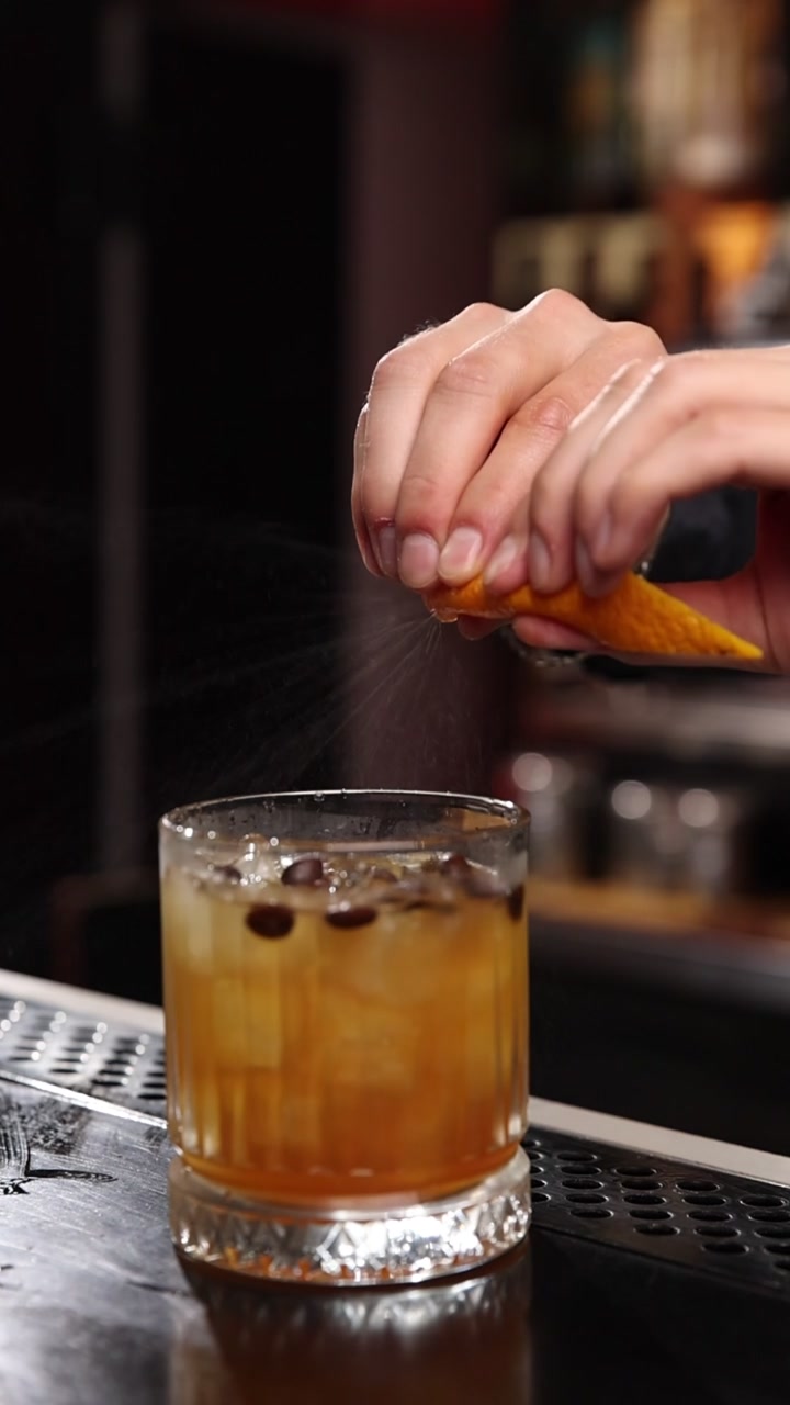 Barman professionista che sprema una scorza d'arancia su un cocktail