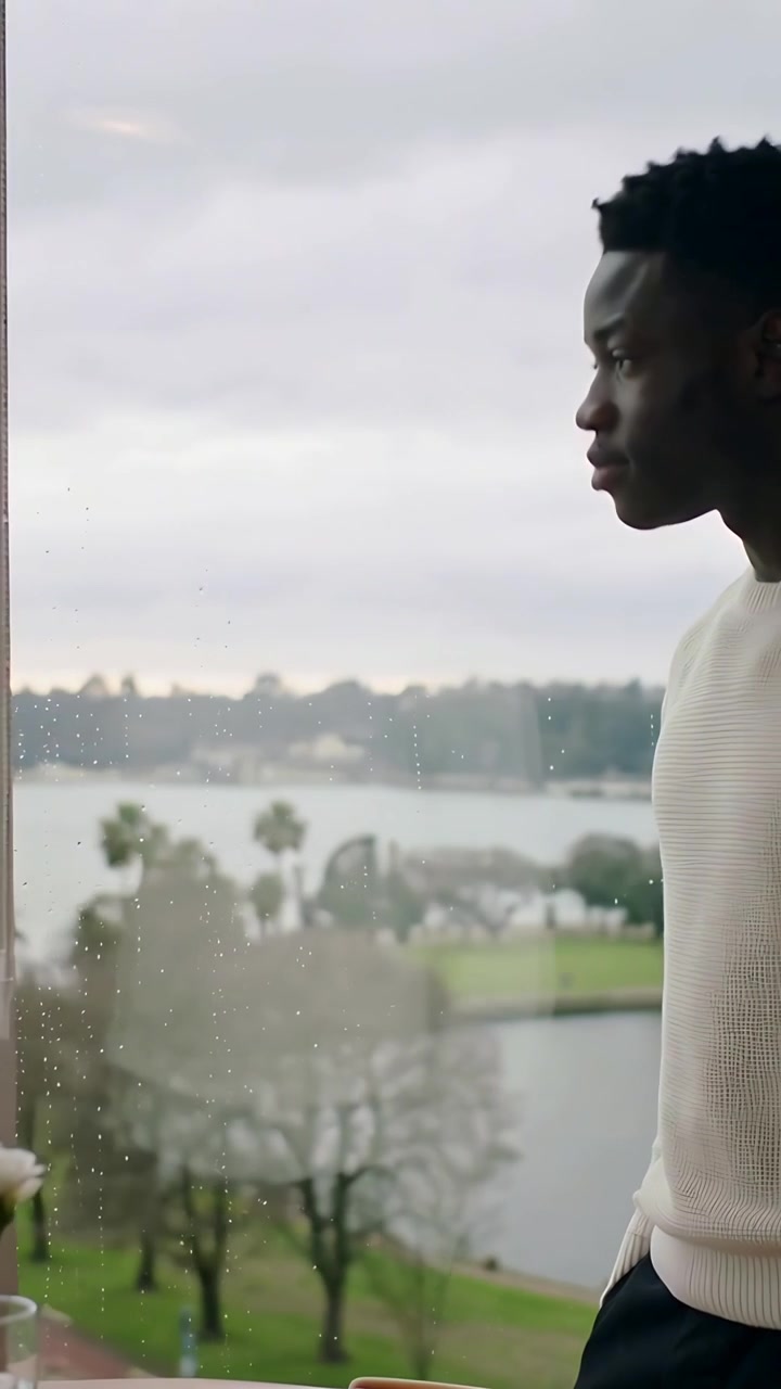 Vertical video: Standing man gazing through wet window at park and water, sweater vase, copy space