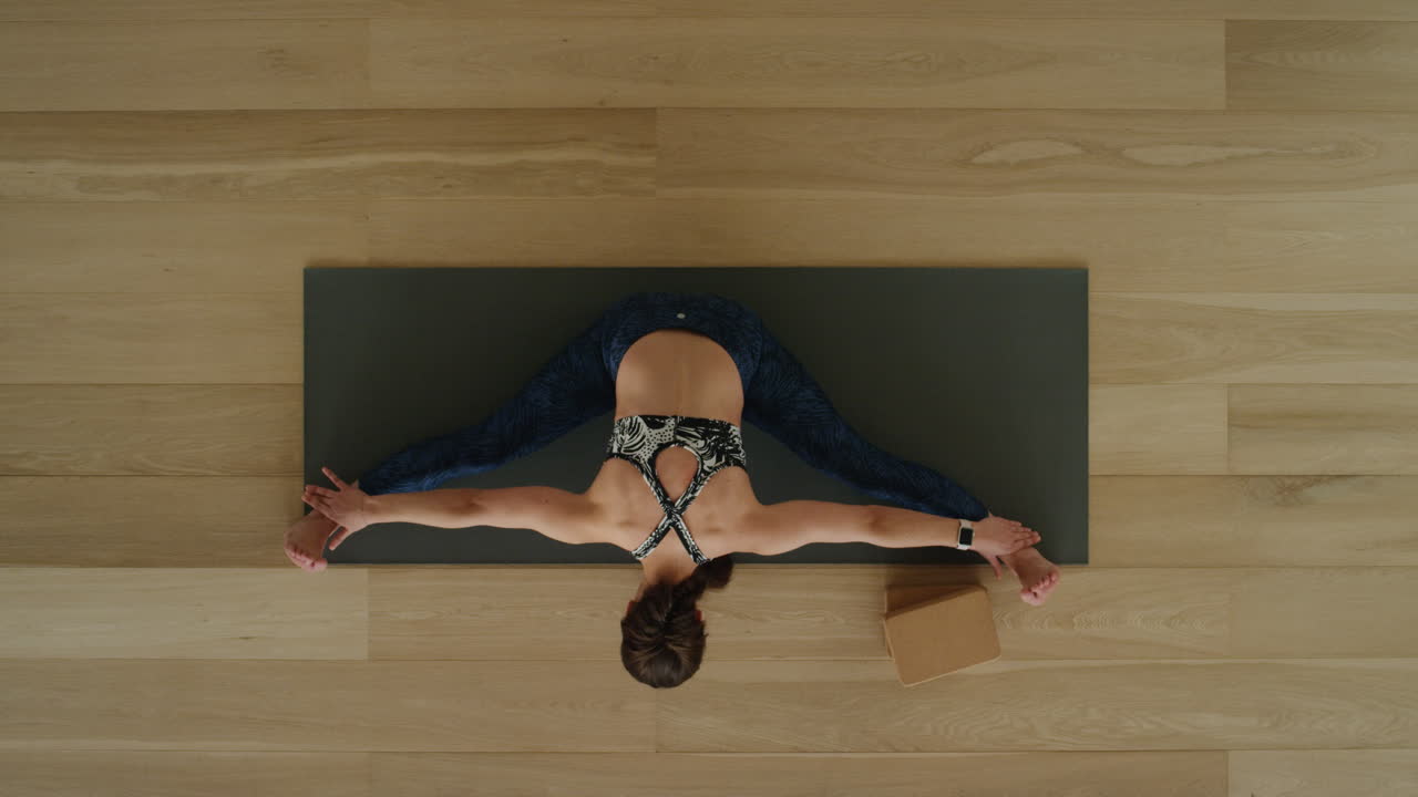 vista superior de una mujer de yoga practicando una pose de curvatura hacia adelante sentada en un estudio de ejercicios disfrutando de un estilo de vida saludable, practicando meditación en una colchoneta de ejercicios.