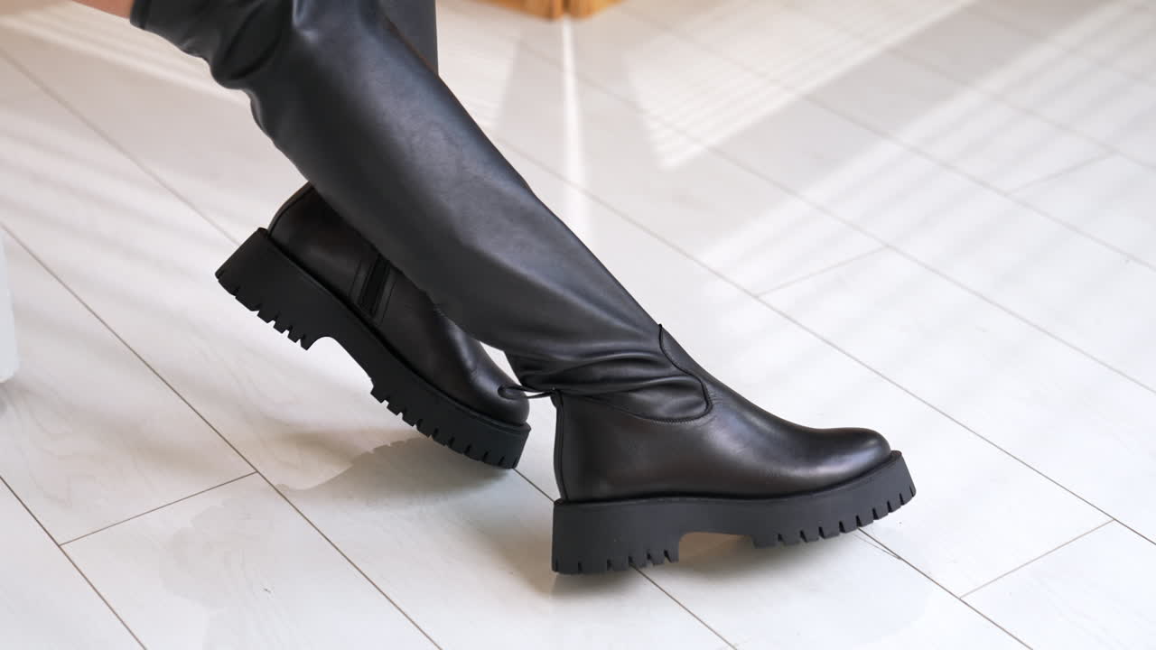 New eco leather boots on massive plain soles. Model demonstrates black autumn footwear sitting in studio. White floor backdrop.