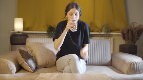 una joven cobarde bebe agua con la mano temblorosa.