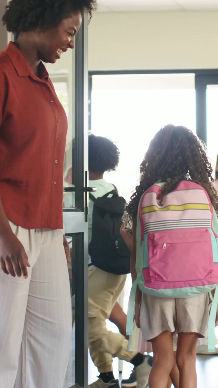 Vertical video: Guiding teacher holding classroom door as kids entering with backpacks, copy space