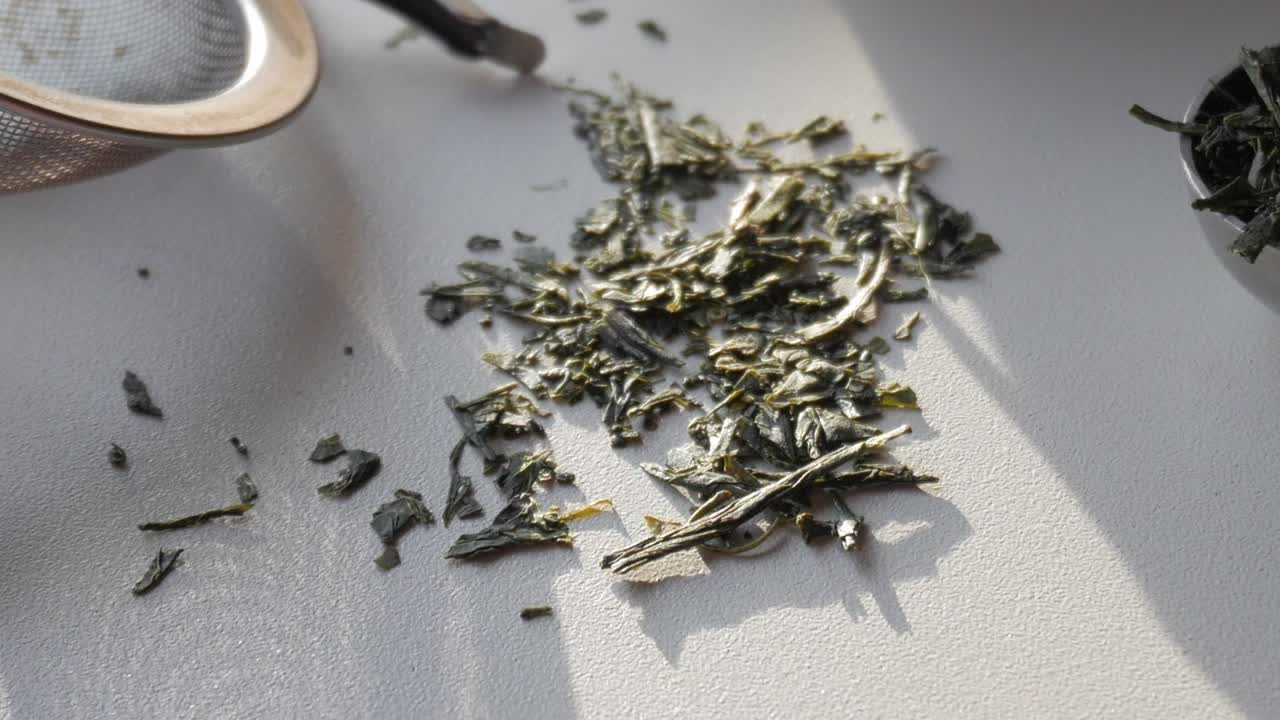 Green tea leaves scattered on a surface with natural light highlighting their texture