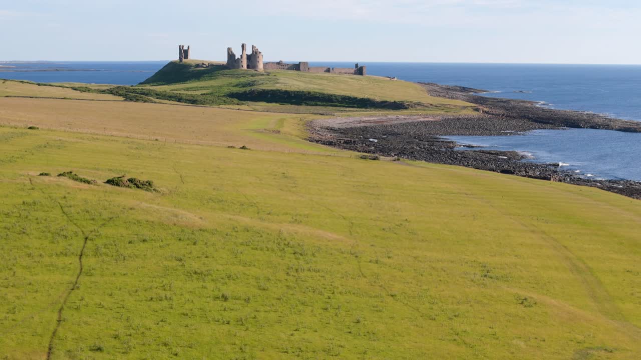Aerial footage of Dunstanburugh castle ruins on a summer morning with no people