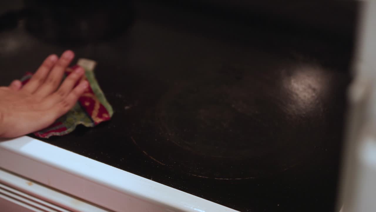 Young South Asian woman's hands wiping down a dirty black stovetop