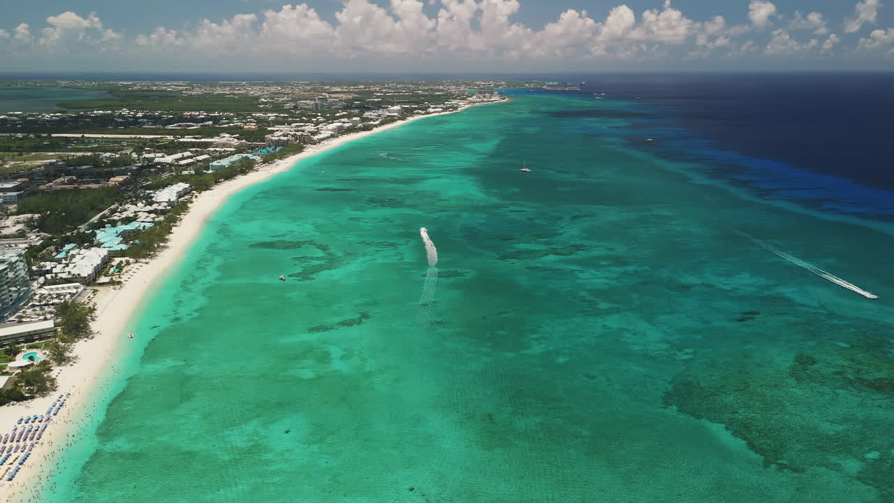 High-altitude aerial follow of a boat driving through the beautiful blue Caribbean water along Seven Mile Beach, Grand Cayman