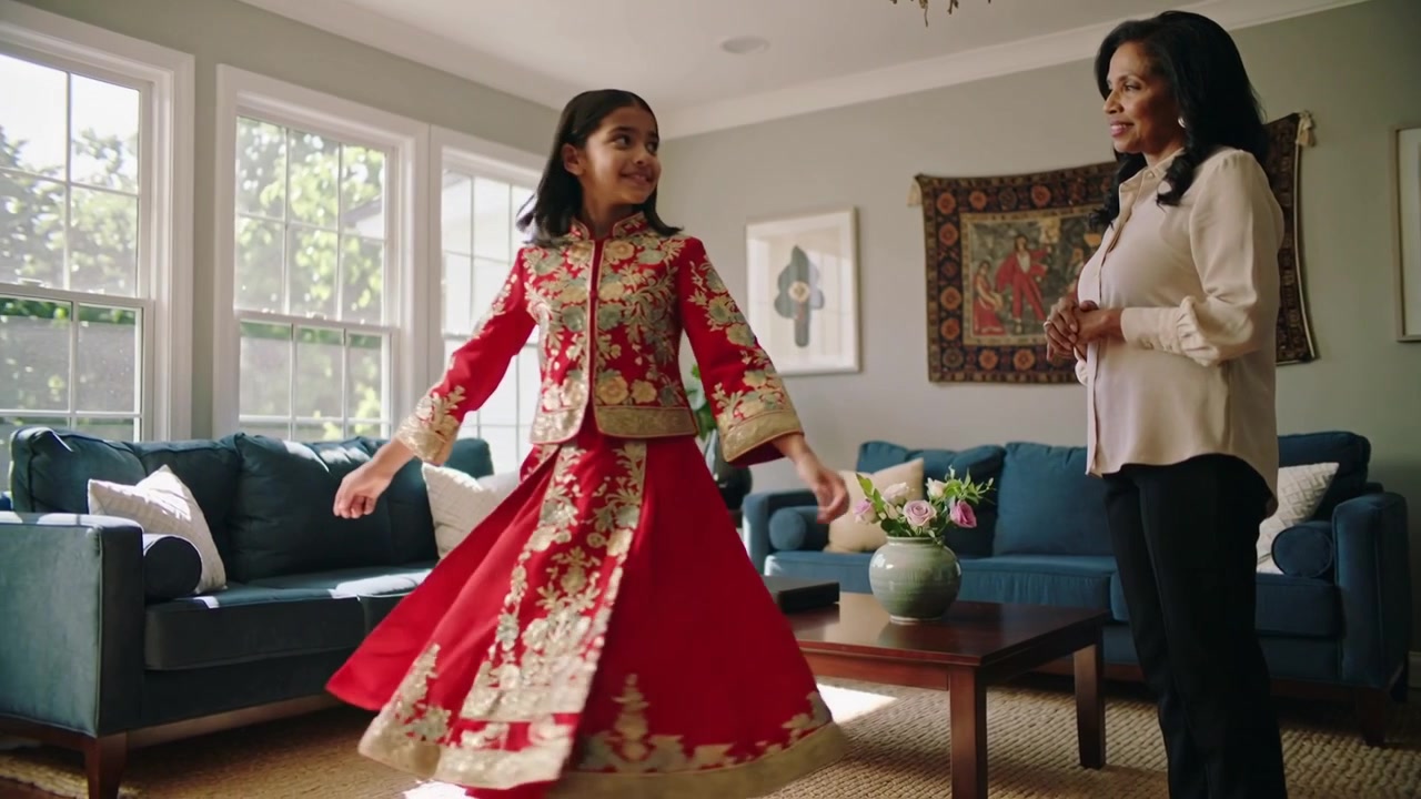 Spinning child in red outfit initiating dance across living room, performing for mom near blue sofa