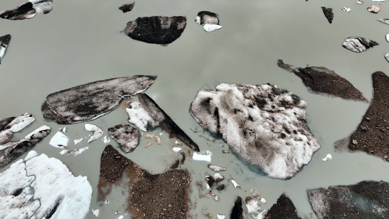 Aerial abstract of broken glacier ice. Top view of fractured glacier ice and dark moraine forming patterns on milky water
