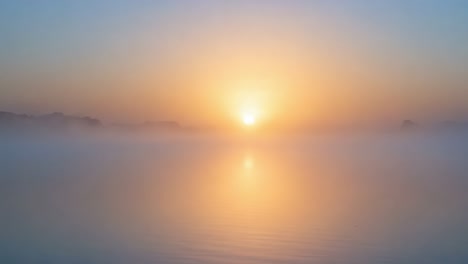 a serene sunrise over a misty lake, capturing the tranquil beauty and soft reflections of early morning light as it breaks through the fog