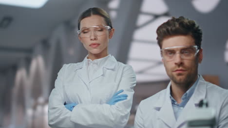 dos médicos serios posando en el laboratorio de microbiología con uniforme de cerca.