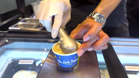 a person scoops ice cream into a cup in a brightly lit shop. the scene captures the precise motion and vibrant colors