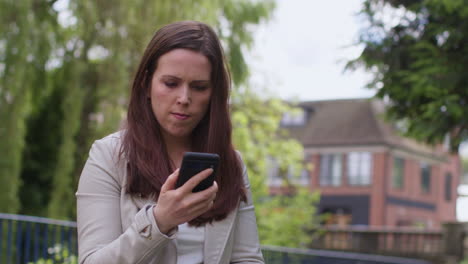 Stressed And Worried Woman Outdoors With Financial Worries About Cost Of Living Crisis Debt And Paying Bills Looking At Mobile Phone Sitting On Bench 2