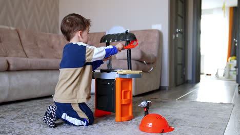 child playing with toy workbench indoors. a young boy kneels on the floor, focused on a colorful toy workbench while using tools in a cozy living room setting