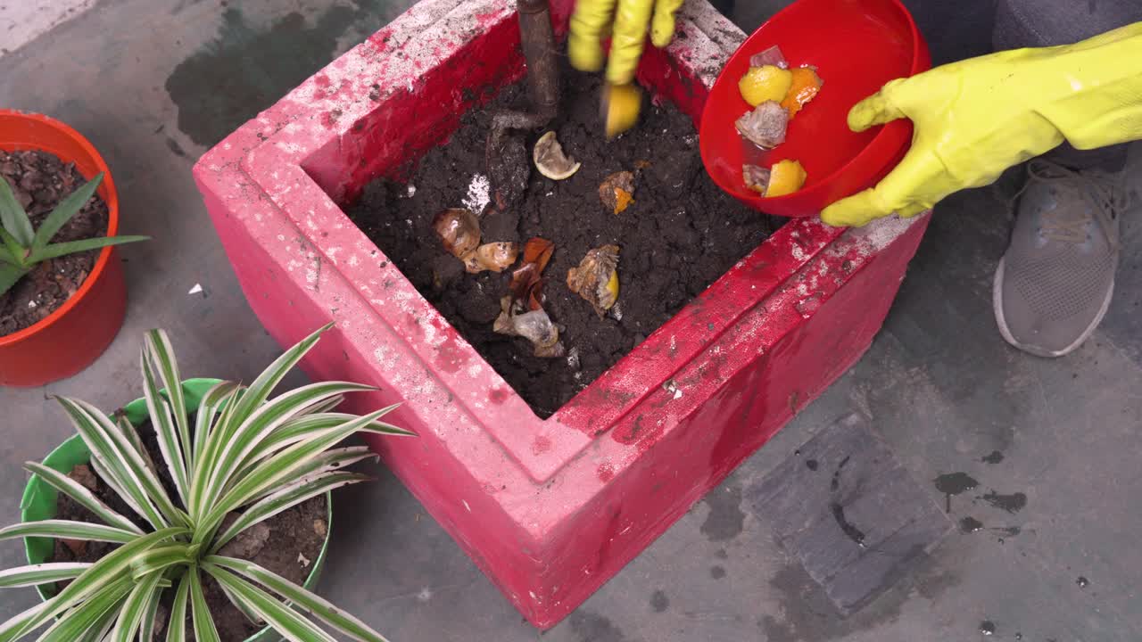 un tipo con guantes amarillos agrega material orgánico a un contenedor de compost en un pequeño jardín del lado de la ciudad