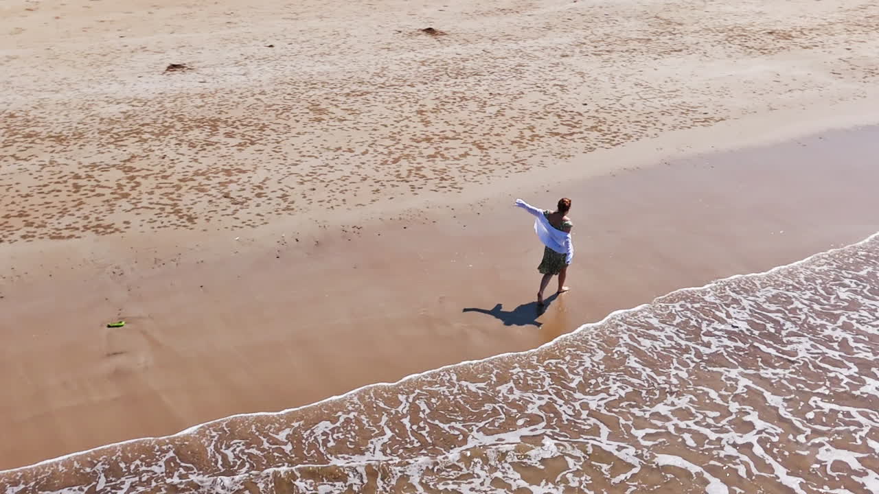 Aerial view around a woman dancing on a tropical beach, sunny day in India