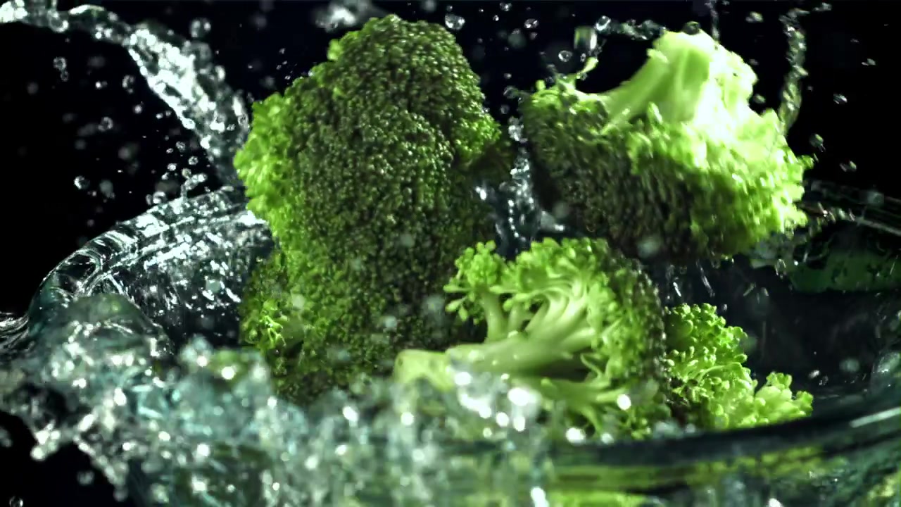 Rallentatore di cimette di broccoli freschi che cadono nell'acqua e schizzano