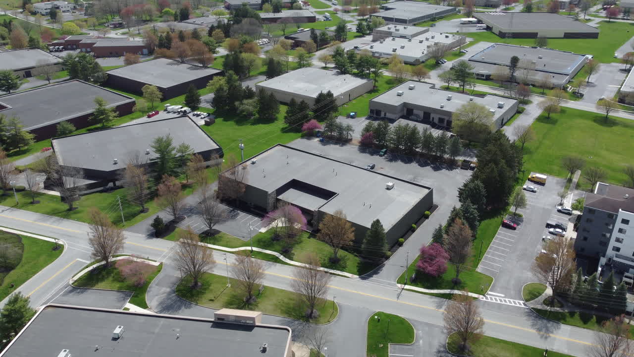 A rotating aerial drone shot captures a quiet commercial park in Lancaster, PA, with low-rise office buildings, blooming spring trees, and spacious parking lots—showcasing suburban business planning.