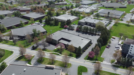 a rotating aerial drone shot captures a quiet commercial park in lancaster, pa, with low-rise office buildings, blooming spring trees, and spacious parking lots—showcasing suburban business planning.
