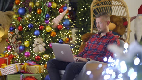 man using laptop near christmas tree
