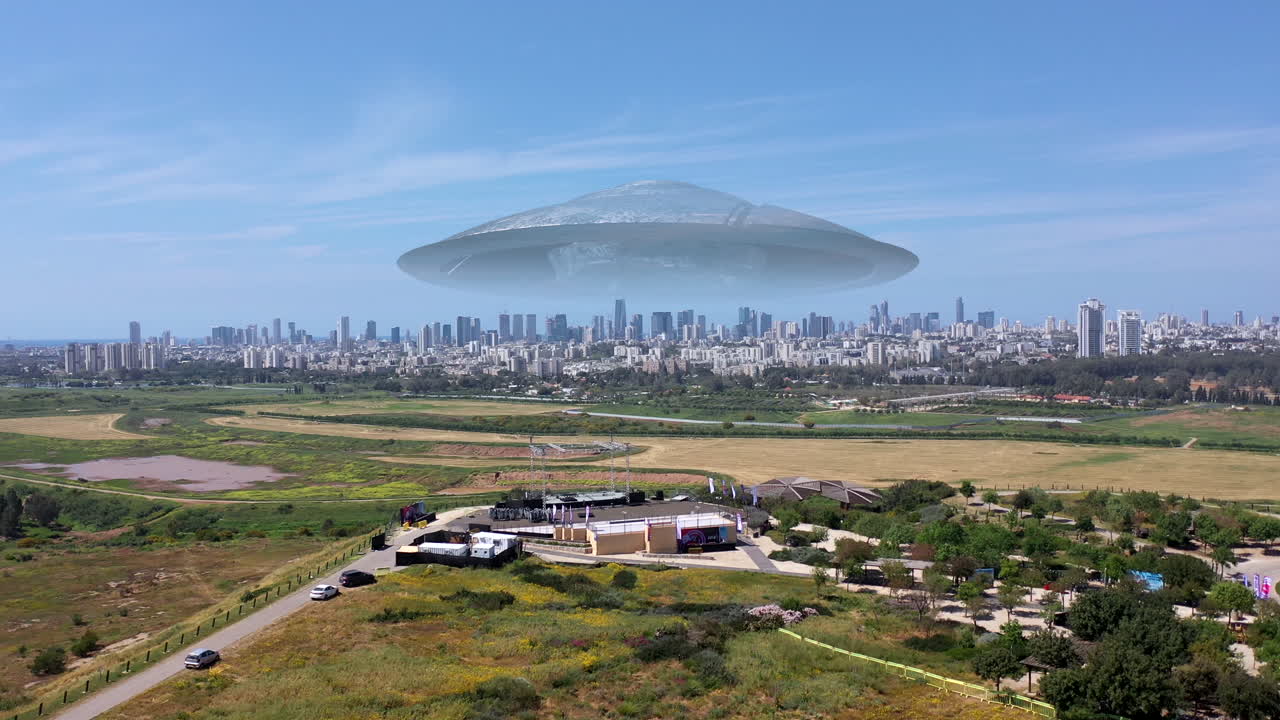 Aerial view of a UFO hovering over a city park with a modern cityscape in the background