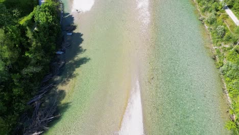 Aerial-shot-of-the-Isar-river-flowing-in-Germany,-revealing-a-bridge,-forest-of-trees,-town-and-mountains-in-the-distance