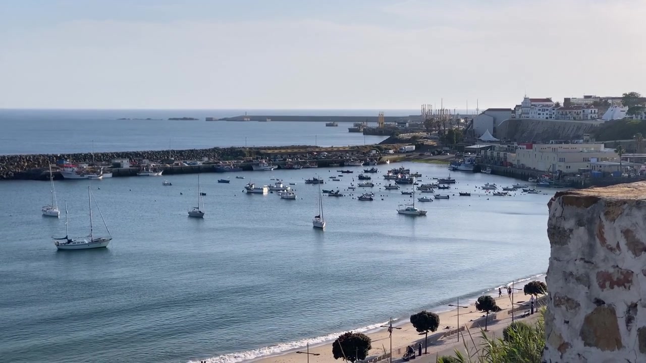 Costa dell'Alentejo, Portogallo, un porto pittoresco pieno di barche da pesca e barche a vela, una spiaggia sabbiosa ed edifici costieri