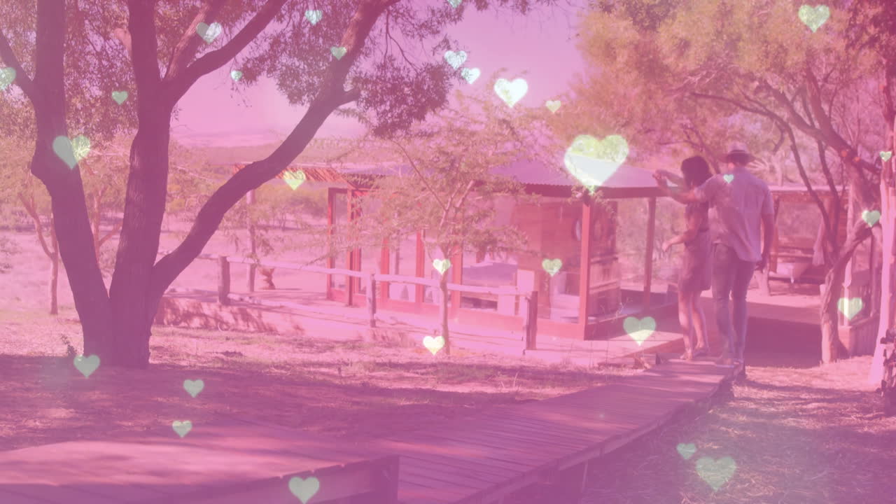 Couple walking on wooden boardwalk through glamping site in tourism ad with floating heart overlays