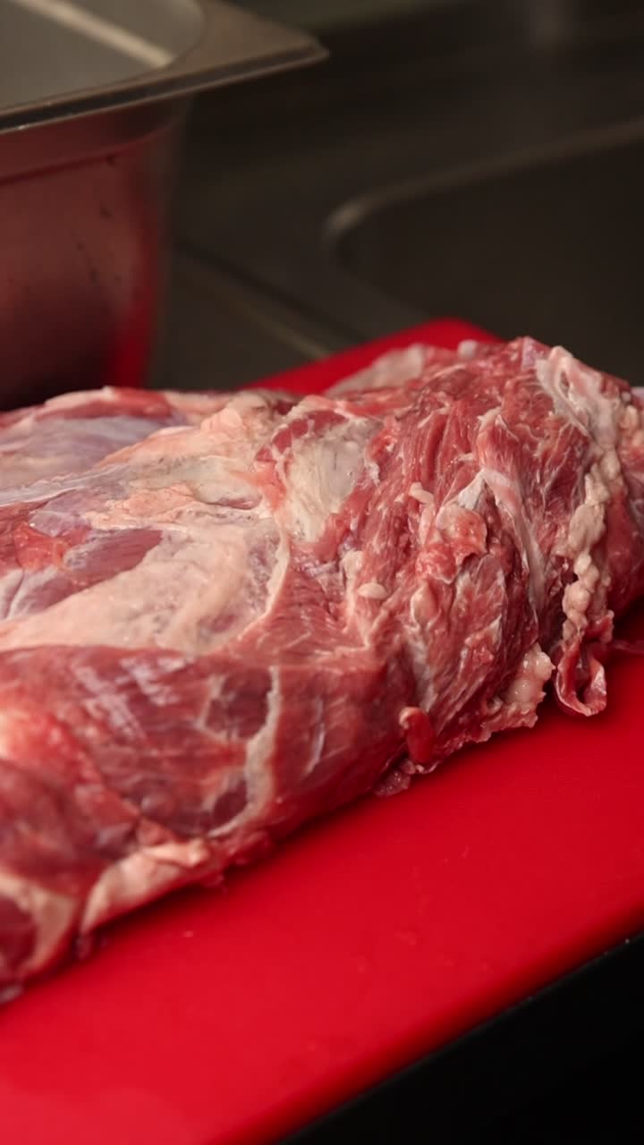 Professional Chef Trimming Raw Meat on a Red Cutting Board