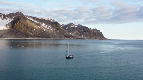 sailing ship with mountain peaks in the background in svalbard islands, norway. aerial drone shot