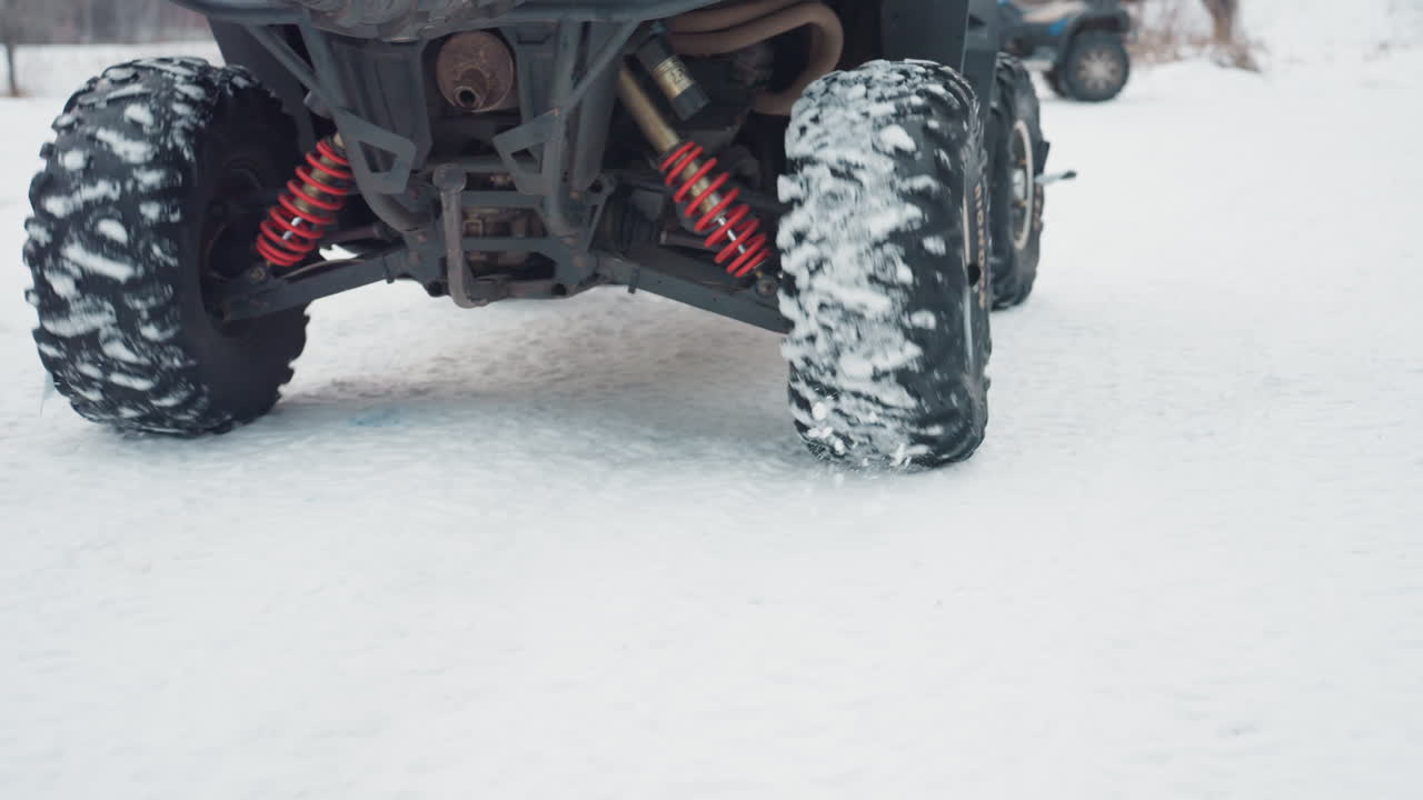 Primo piano di aderenza e sospensione. Meccanico che esamina la trazione dei pneumatici su superficie ghiacciata. Scena invernale che mostra i pneumatici dell'ATV che aderiscono alla neve con i componenti delle sospensioni a fuoco e battistrada in gomma testurizzati.