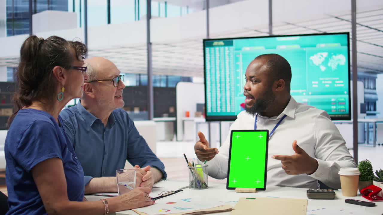 Adviser shows green screen on a tablet to middle aged people in modern office