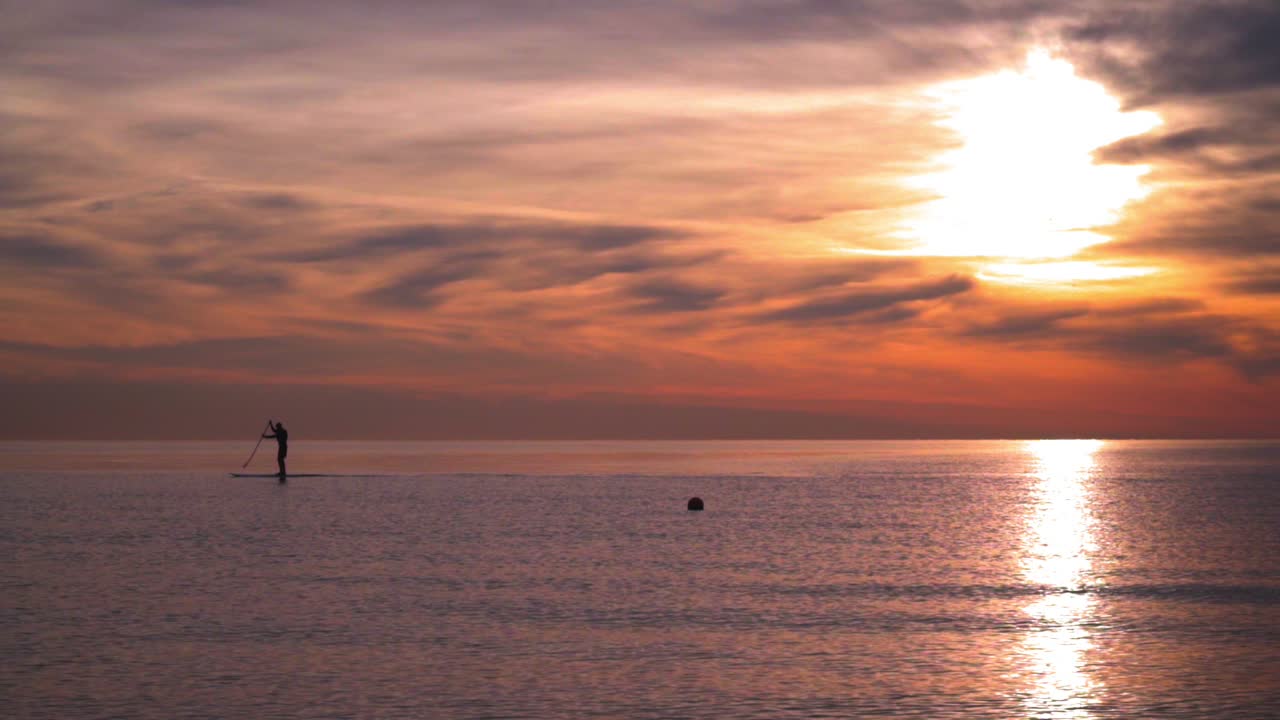 silueta de un hombre en una tabla de surf en el mar al atardecer. mar al atardecer. reflejo del sol