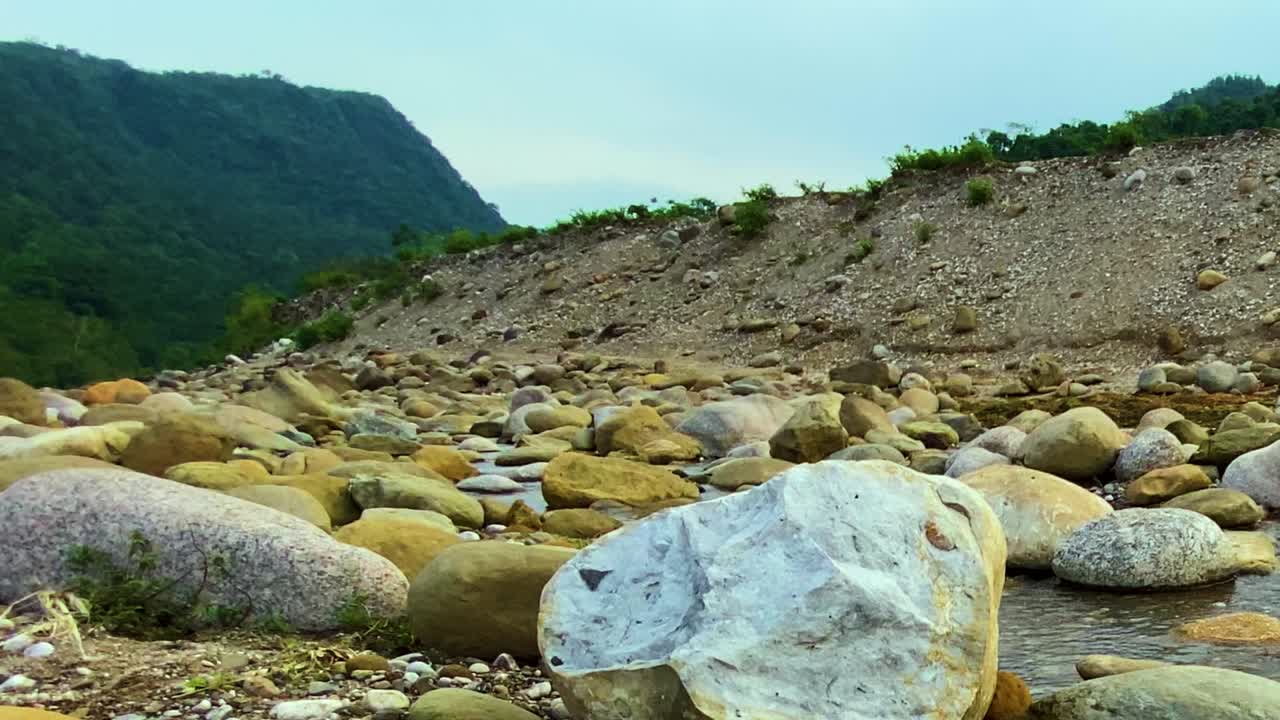 Panning a destra attraverso il letto roccioso e asciutto di un fiume con un ruscello poco profondo a Sylhet, Bangladesh