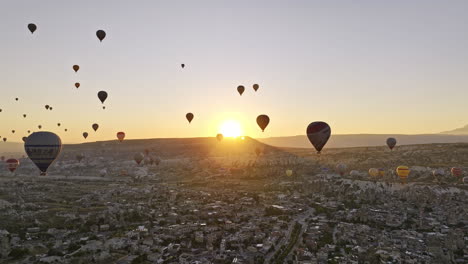 Göreme-Turkey-Aerial-v57-magical-landscape-view-of-volcanic-rock-formations-with-glowing-sun-rising-up-above-mesa-tabletop-mountain-against-the-cappadocian-horizon---Shot-with-Mavic-3-Cine---July-2022