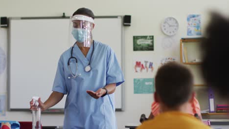 mixed race female medical worker wearing face mask showing schoolchildren how to disinfect hands