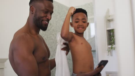 african american father and son flexing their muscles in mirror taking selfie together