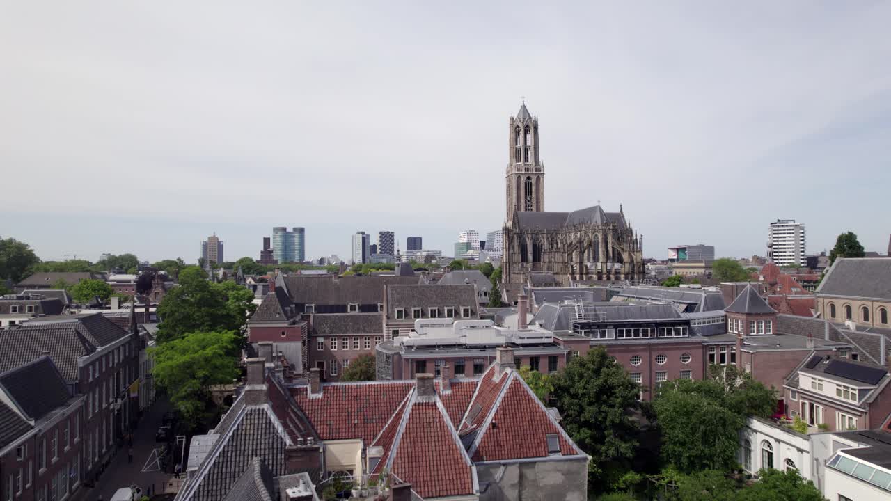 Descending aerial revealing historic city center buildings beneath Utrecht gothic architecture of diocese ambulatory with modern high rise buildings on the horizon behind