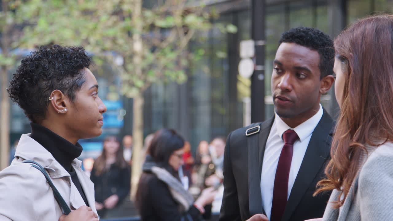 Three millennial business colleagues standing on a busy city street talking, close up