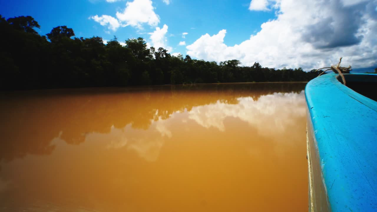 vista desde una lancha a motor navegando rápidamente en el río kinabatangan en malasia, el cielo es azul y nublado, el reflejo del cielo en el agua