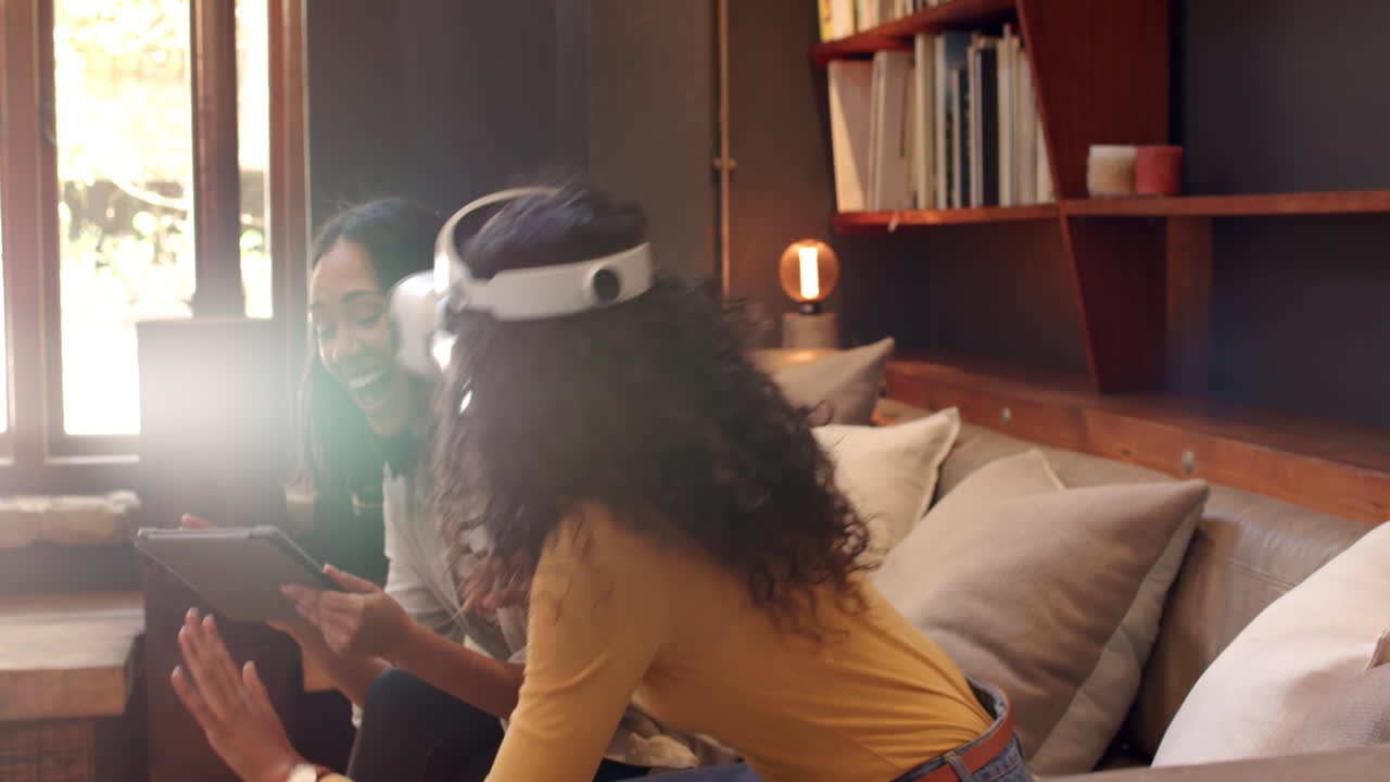 Multiracial female friends enjoying virtual reality experience at home, smiling and using tablet