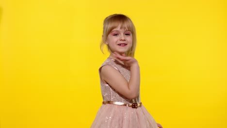 Little-smiling-blonde-child-kid-girl-waving-greeting,-hello-or-bye-with-hand-on-yellow-background