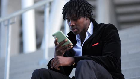 Young-African-Businessman-in-a-Black-Suit,-Recording-a-Voice-Message-on-Stairs