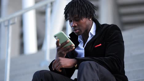 young african businessman in a black suit, recording a voice message on stairs